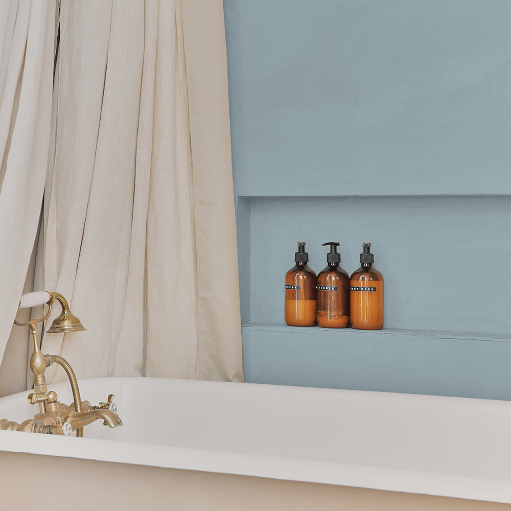 Bathroom with grey-blue panelled wall in Lie-in by COAT Paints, with bathtub and amber bottles