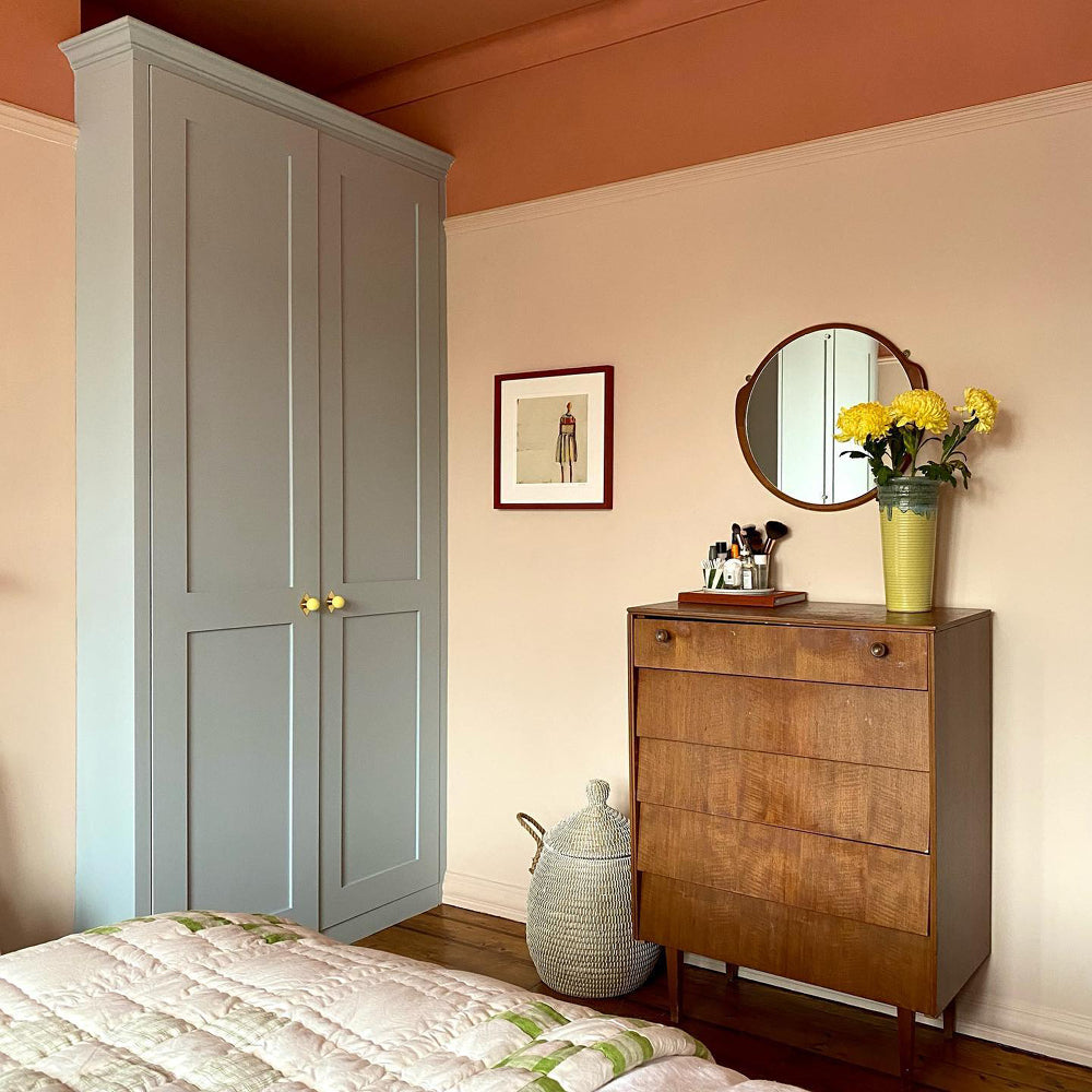 Bedroom with grey-blue wardrobe in Lie-in by COAT Paints, warm terracotta ceiling and wooden dresser
