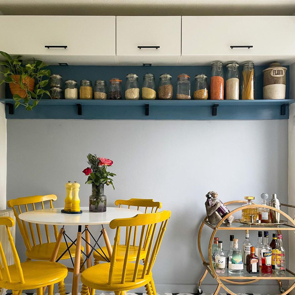 Kitchen-diner with grey-blue walls in Lie-in by COAT Paints, with yellow chairs and pantry shelves