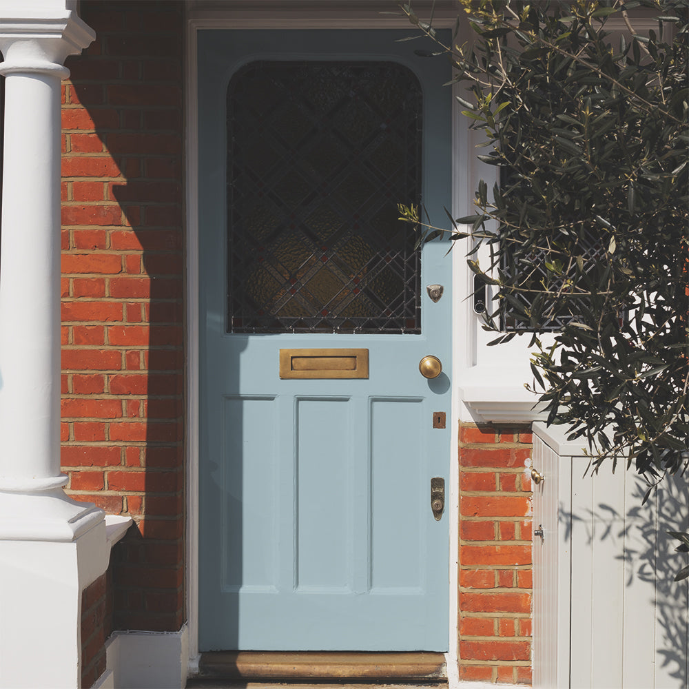Front door painted in Lie-in, a soft grey-blue exterior paint by COAT Paints, on red brick terrace